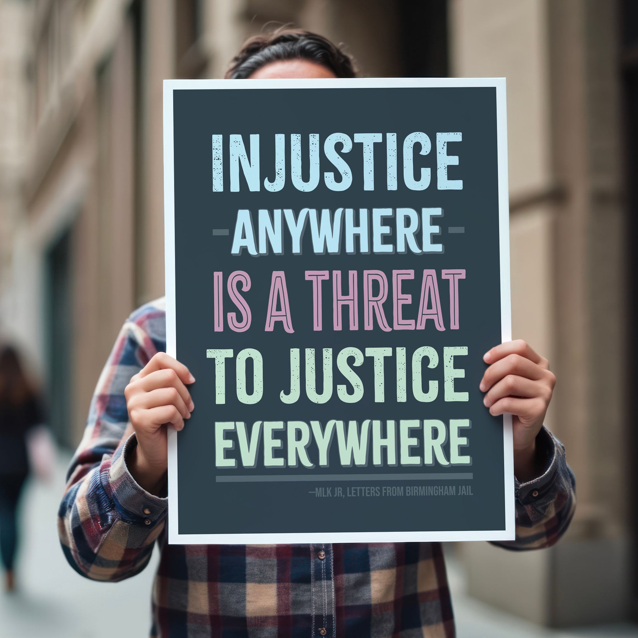 Person holding protest sign with quote from Martin Luther King Jr that reads "injustice anywhere is a threat to justice everywhere" in colorful bold distressed text.