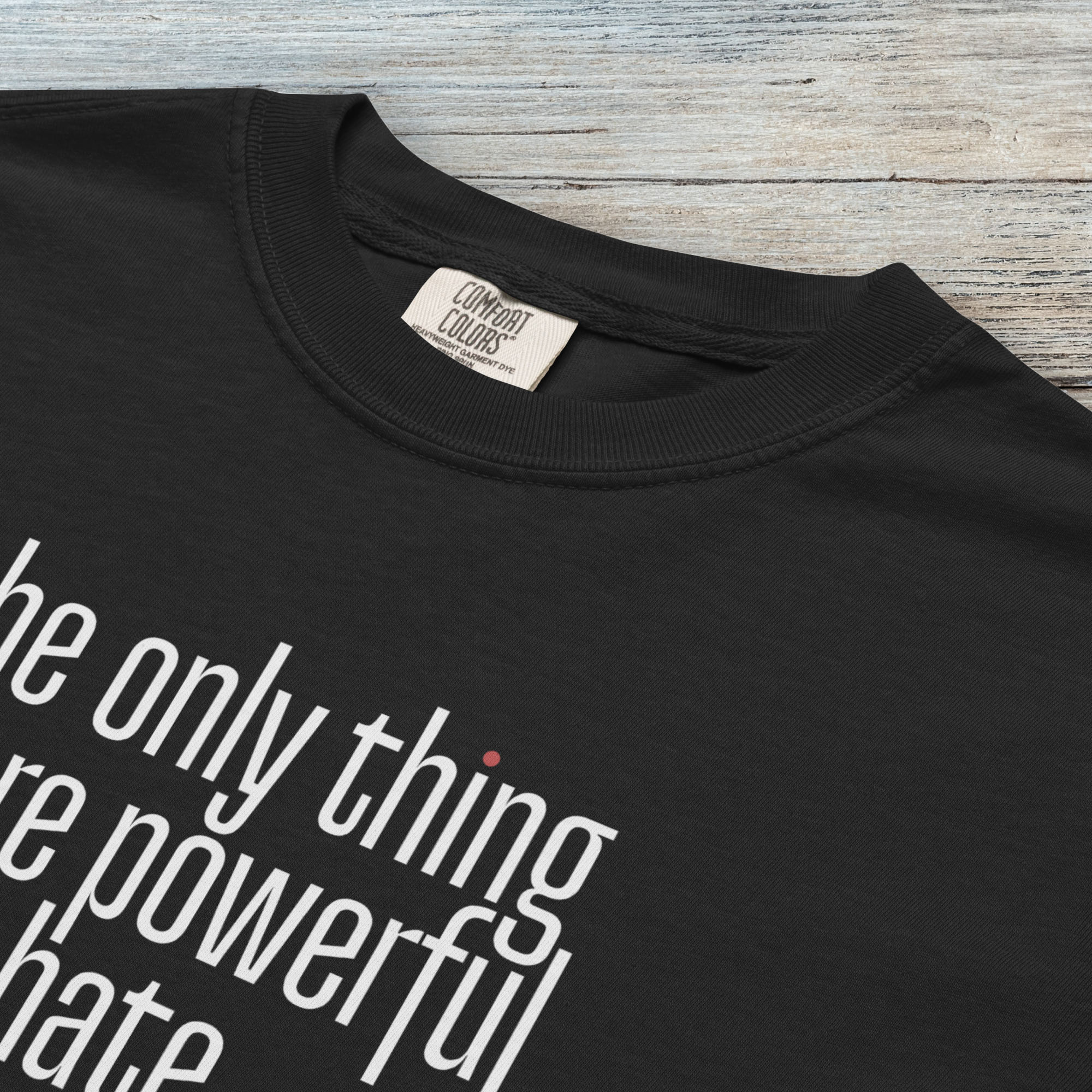 Closeup detail of black t-shirt with a stylized text block reading “the only thing more powerful than hate is love."