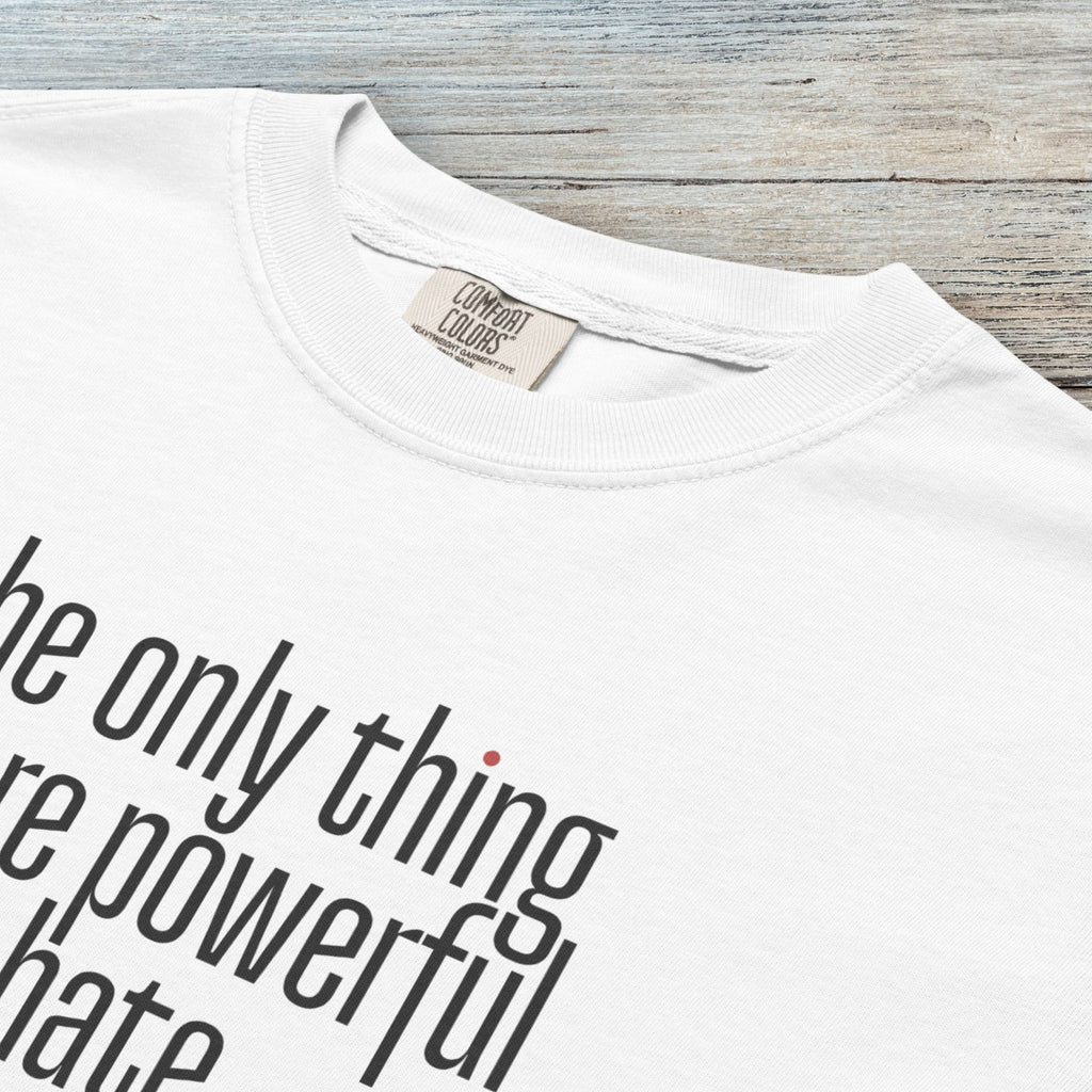 Closeup detail of white t-shirt with a stylized text block reading “the only thing more powerful than hate is love."