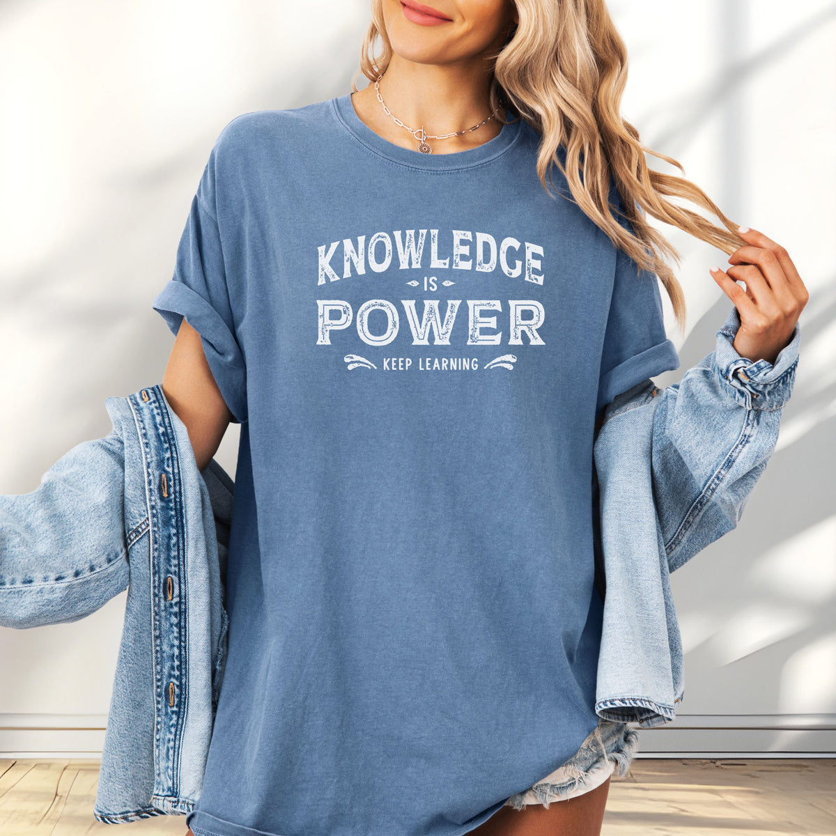 Female model wearing oversized blue jean t-shirt with vintage style typography reading “Knowledge Is Power – Keep Learning."