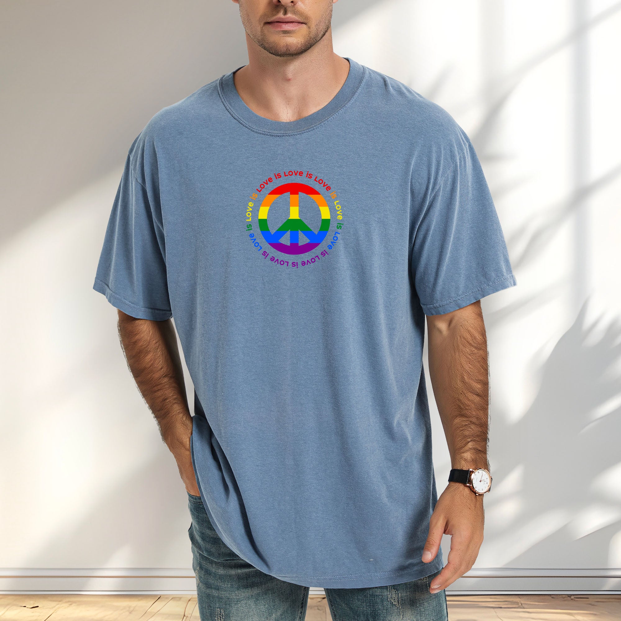 Male model wearing blue jean t-shirt with LGBTQ pride graphic — a peace sign in the LGBTQ flag colors, with the text 