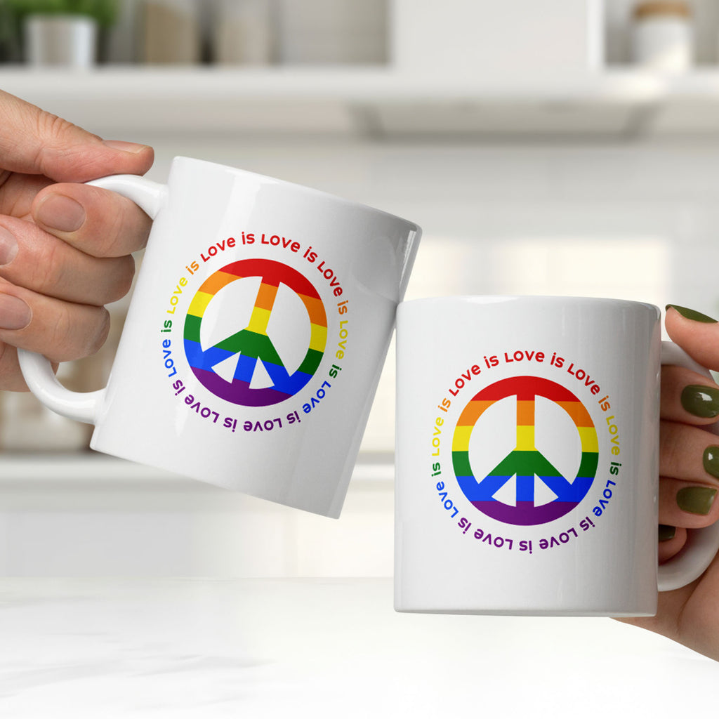 Two people holding ceramic coffee mug with a peace sign in the colors of the LGBTQ+ flag, surrounded by repeated "love is love" text. They are clinking the mugs together, showing graphic on both sides of the mug.