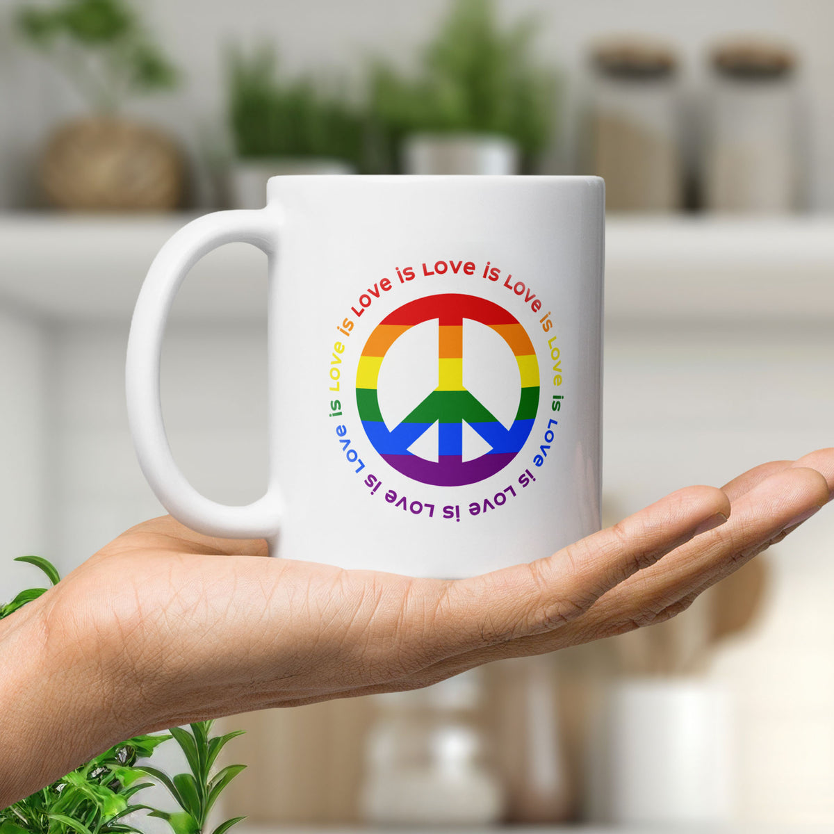 White ceramic coffee mug with a peace sign in the colors of the LGBTQ+ flag, surrounded by repeated "love is love" text. held in the palm of a hand.