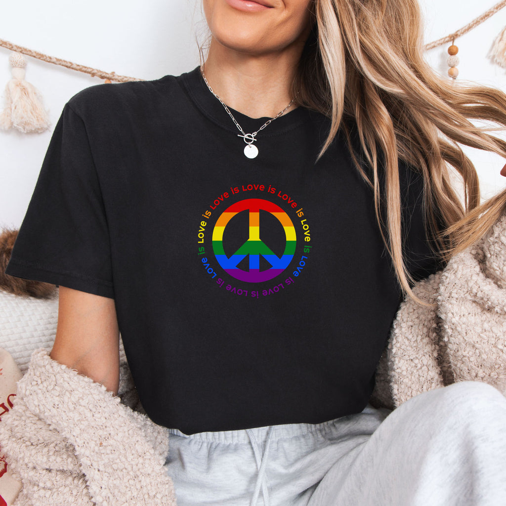 Female model wearing black t-shirt with LGBTQ pride graphic — a peace sign in the LGBTQ flag colors, with the text "love is love" repeated in a circle around the peace sign.