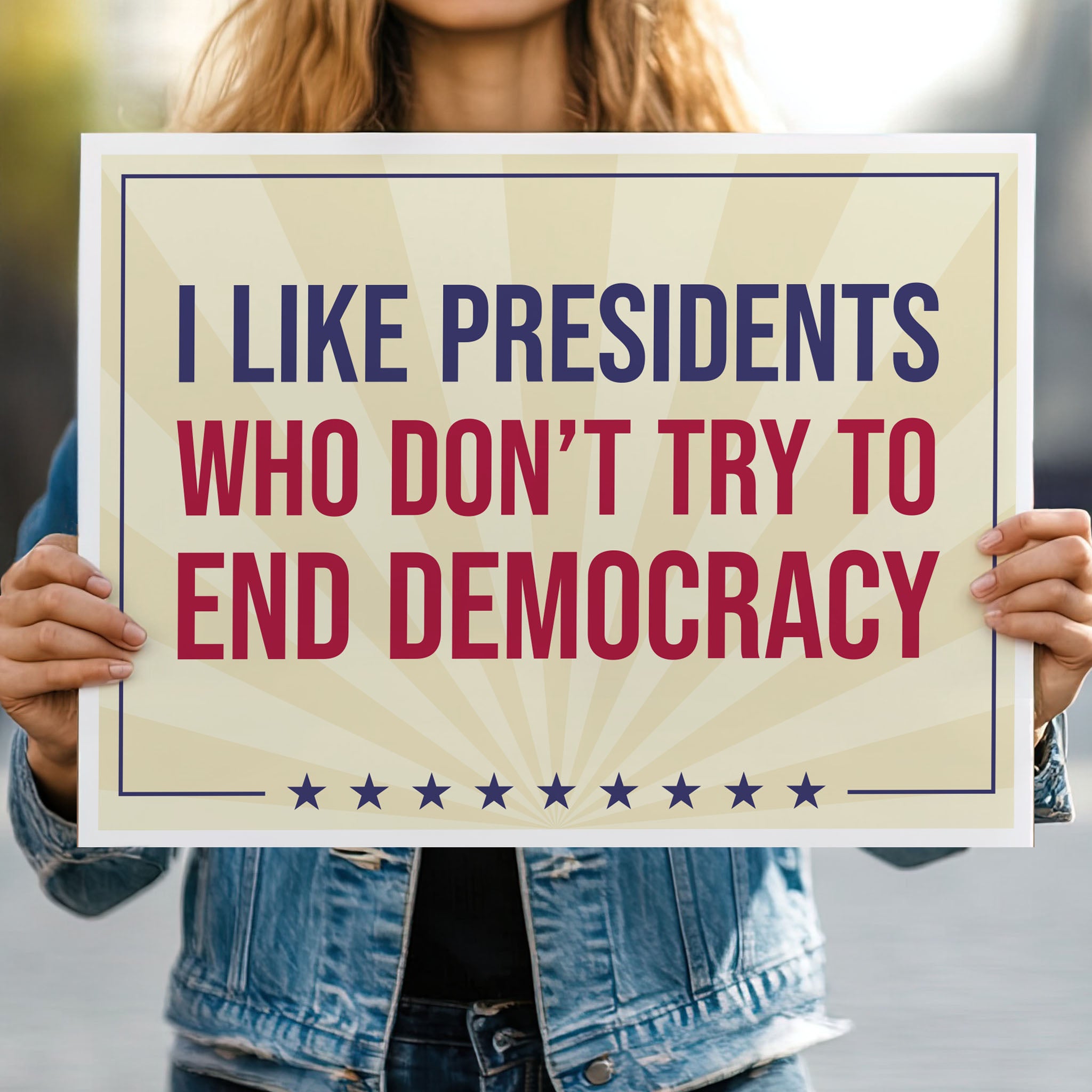Person holding protest sign with light gold background and red and blue bold text that reads "I like presidents who don't try to end democracy."