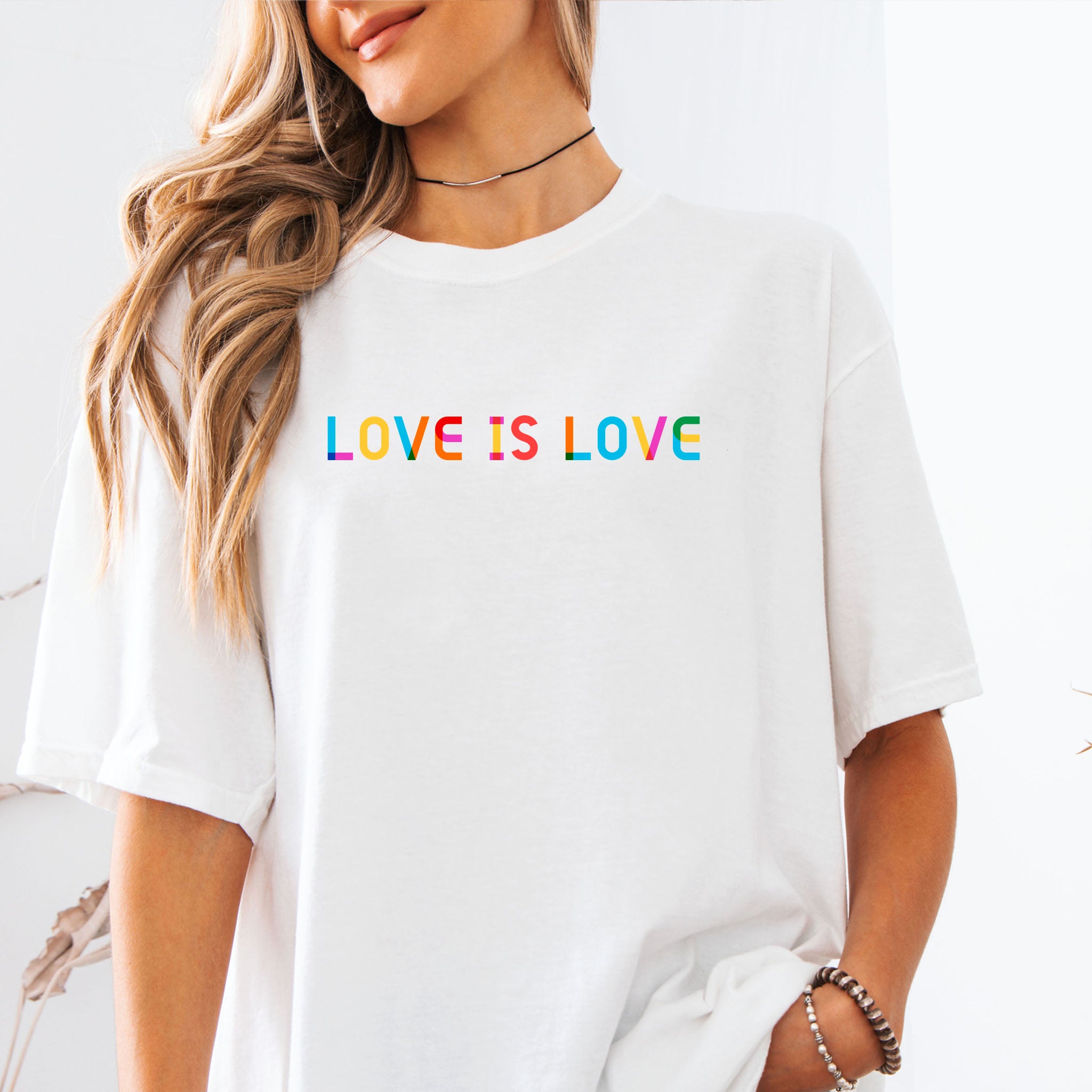 Female model wearing white t-shirt with rainbow “love is love” text designed in the Gilbert font.