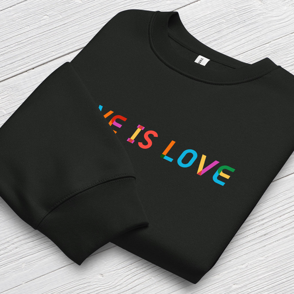 Folded black Bella+Canvas crewneck sweatshirt with rainbow “love is love” text designed in the Gilbert font, showing cuff detail.