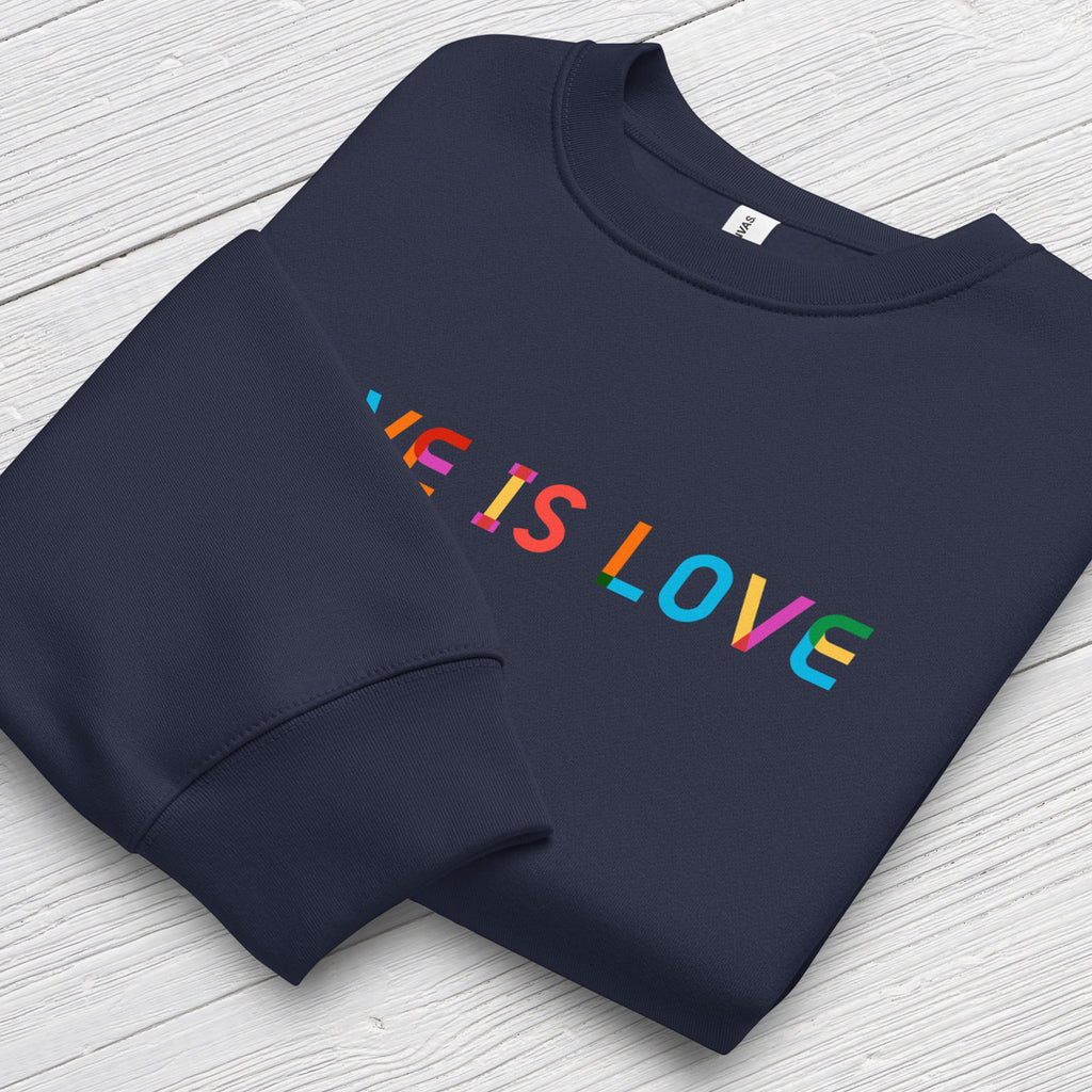 Folded navy Bella+Canvas crewneck sweatshirt with rainbow “love is love” text designed in the Gilbert font, showing cuff detail.