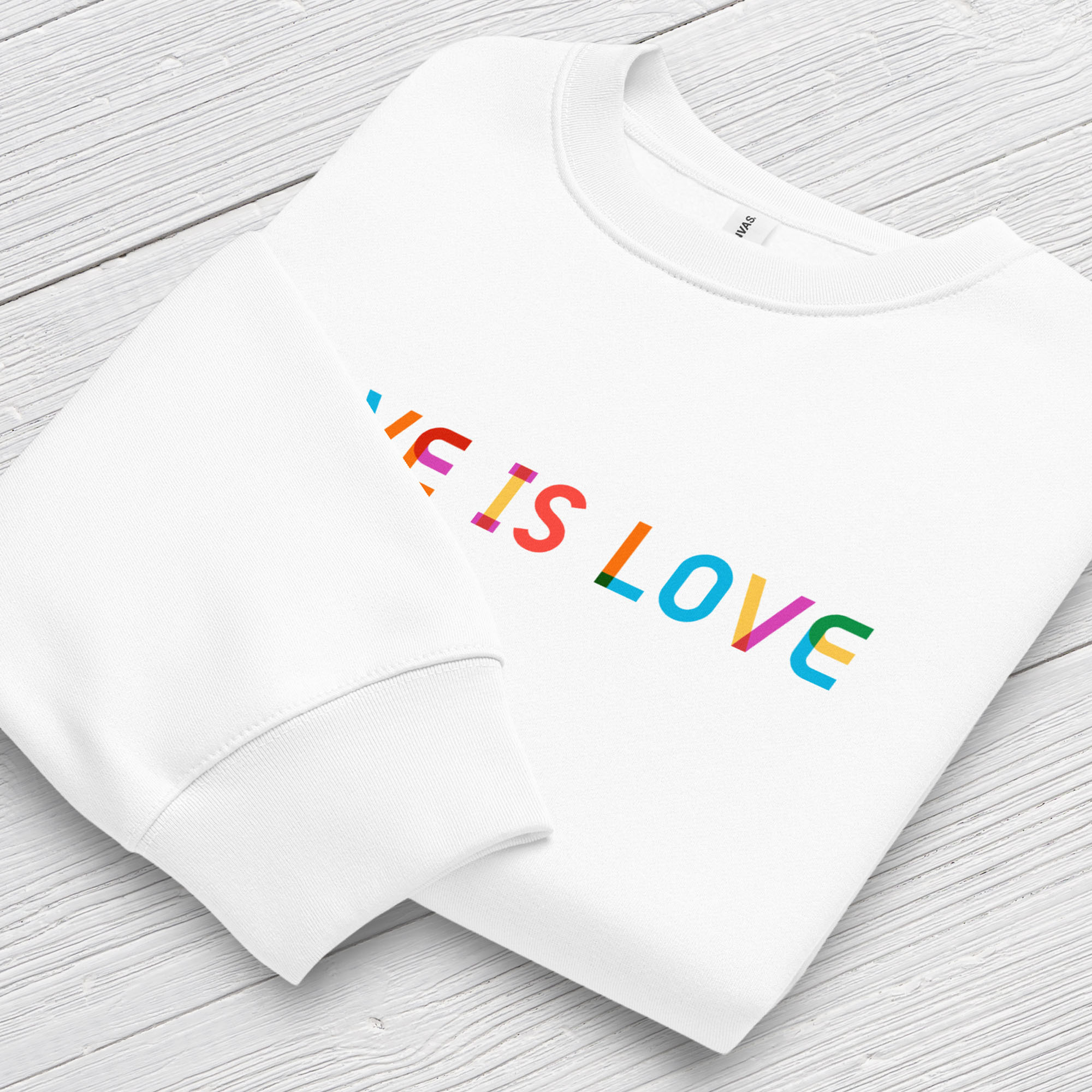 Folded white Bella+Canvas crewneck sweatshirt with rainbow “love is love” text designed in the Gilbert font, showing cuff detail.