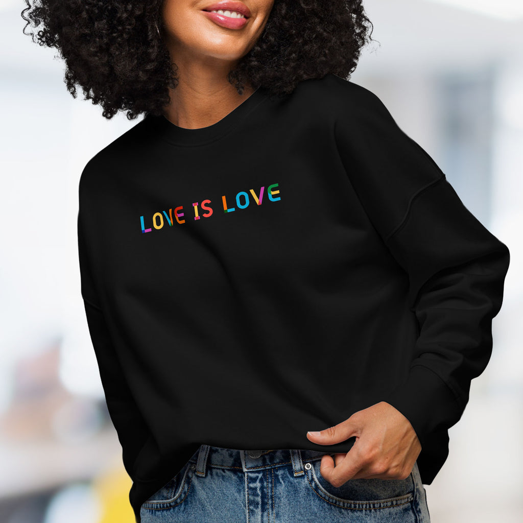 Female model wearing black women's crewneck sweatshirt with rainbow “love is love” text designed in the Gilbert font.