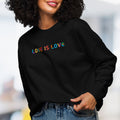 Female model wearing black women's crewneck sweatshirt with rainbow “love is love” text designed in the Gilbert font.