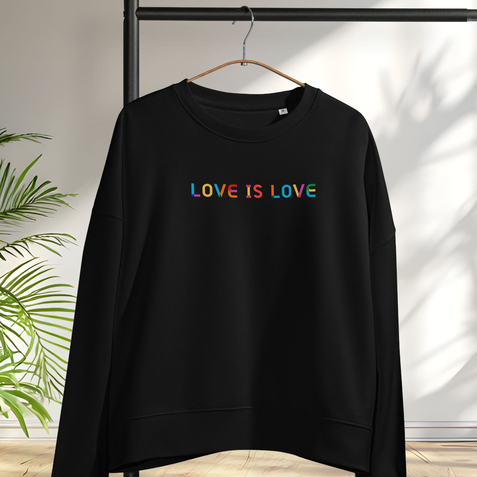 Hanging black women's crewneck sweatshirt with rainbow “love is love” text designed in the Gilbert font.