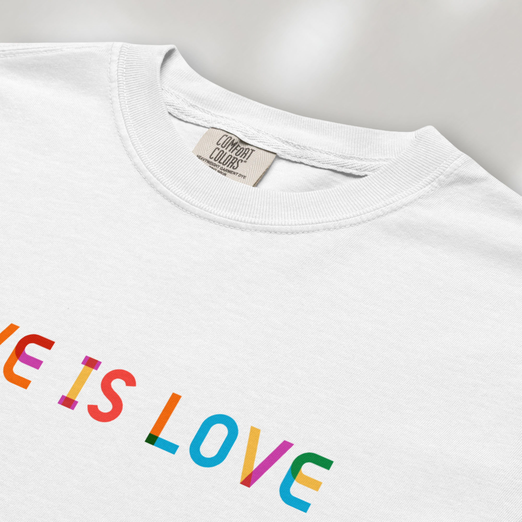 Closeup detail of white oversized t-shirt with rainbow “love is love” text in a single line.