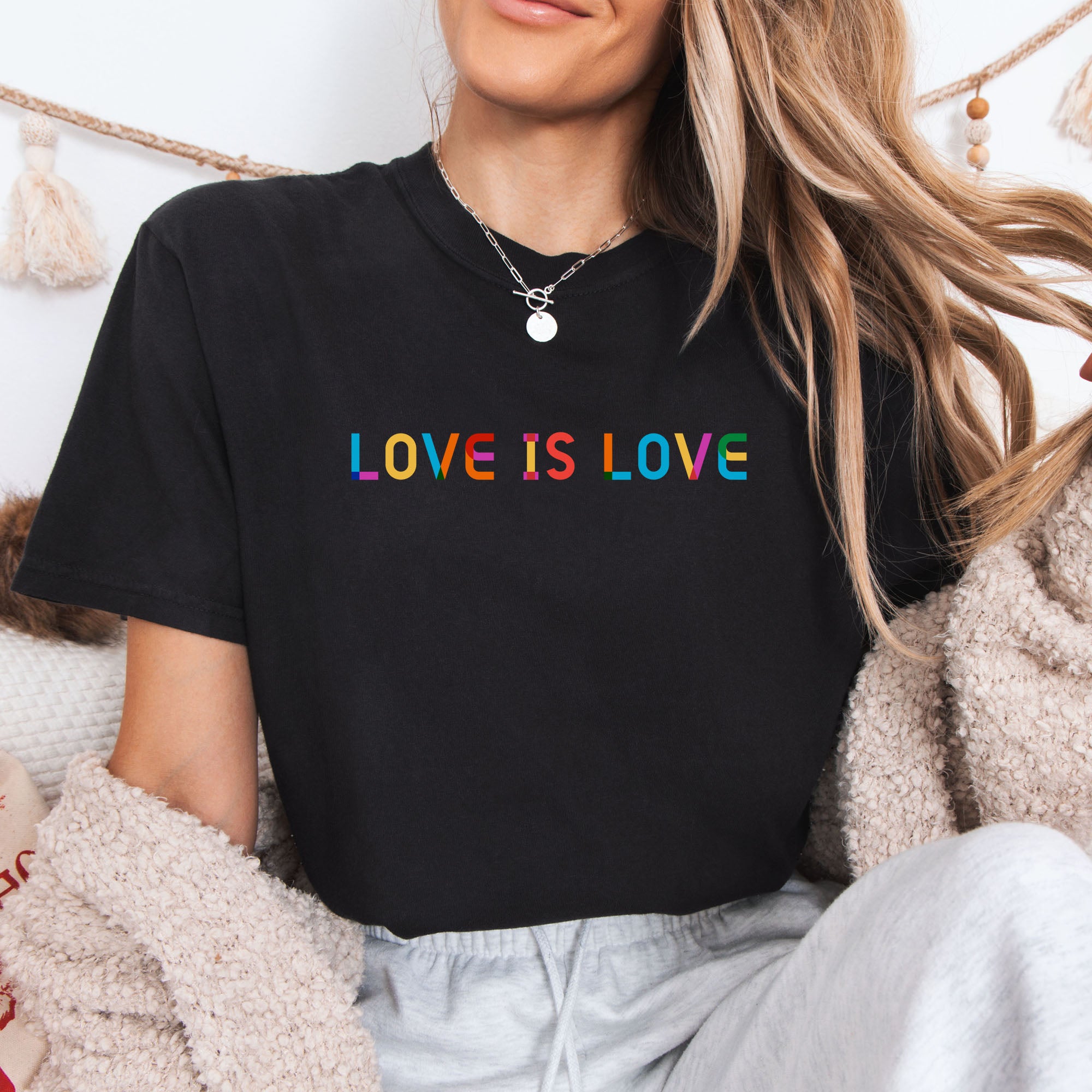 Female model wearing black oversized t-shirt with rainbow “love is love” text in a single line.