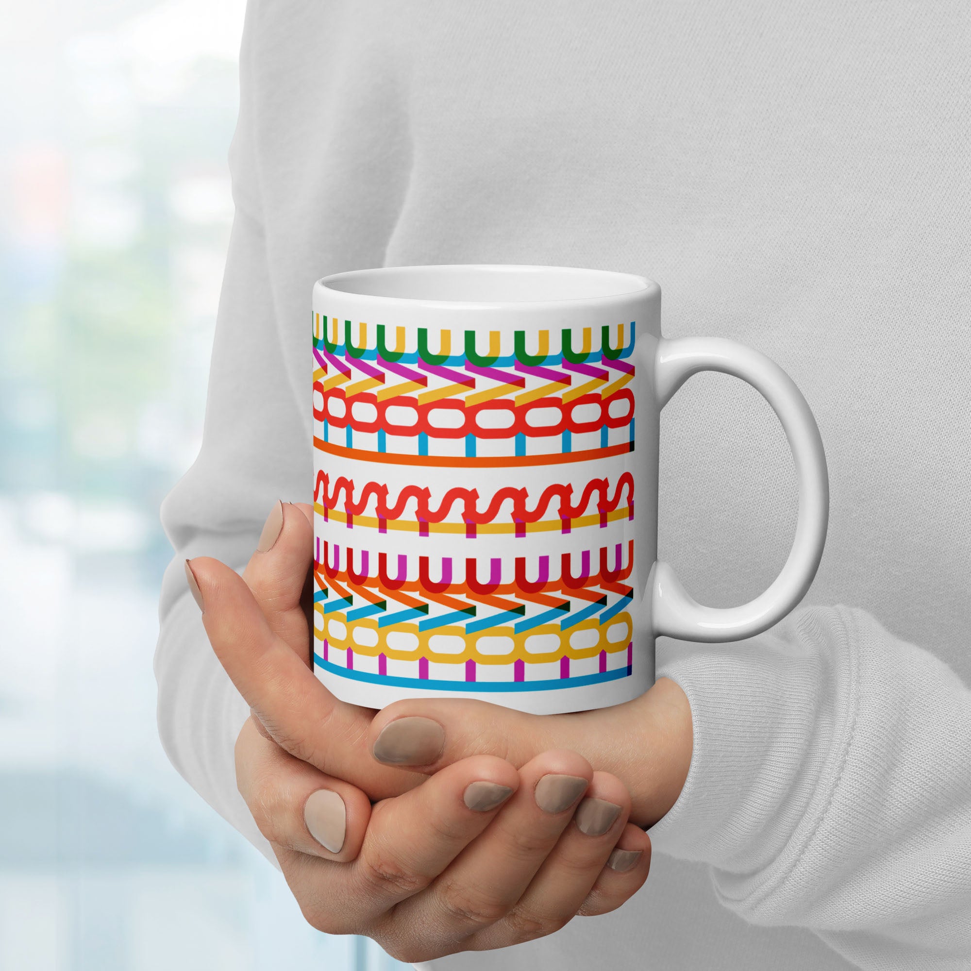 Person holding colorful coffee mug with a repeating hidden “love is love” message in the Gilbert font, featuring bright rainbow-inspired patterns wrapped around the mug.