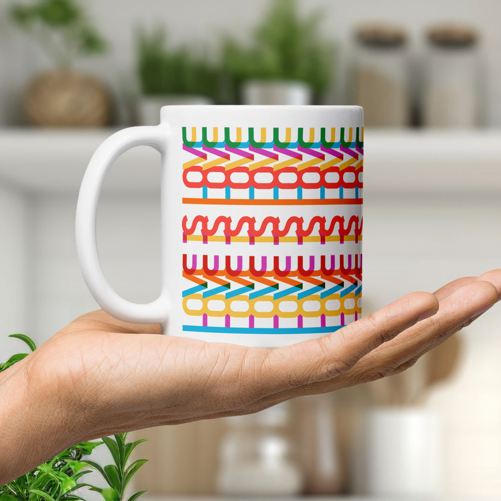 Colorful coffee mug with a repeating hidden “love is love” message in the Gilbert font, featuring bright rainbow-inspired patterns wrapped around the mug, resting in the palm of a hand.