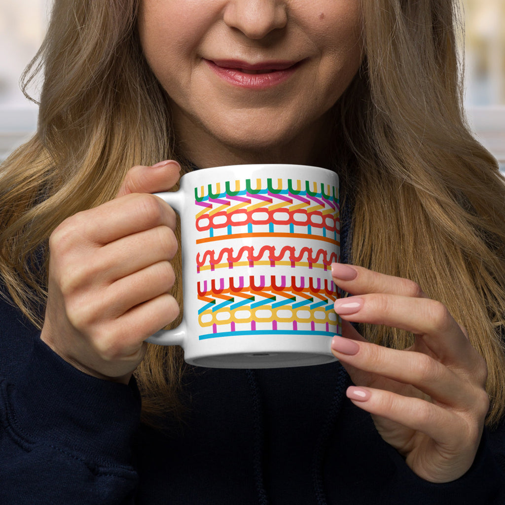 Woman about to take a sip from a colorful coffee mug with a repeating hidden “love is love” message in the Gilbert font, featuring bright rainbow-inspired patterns wrapped around the mug.