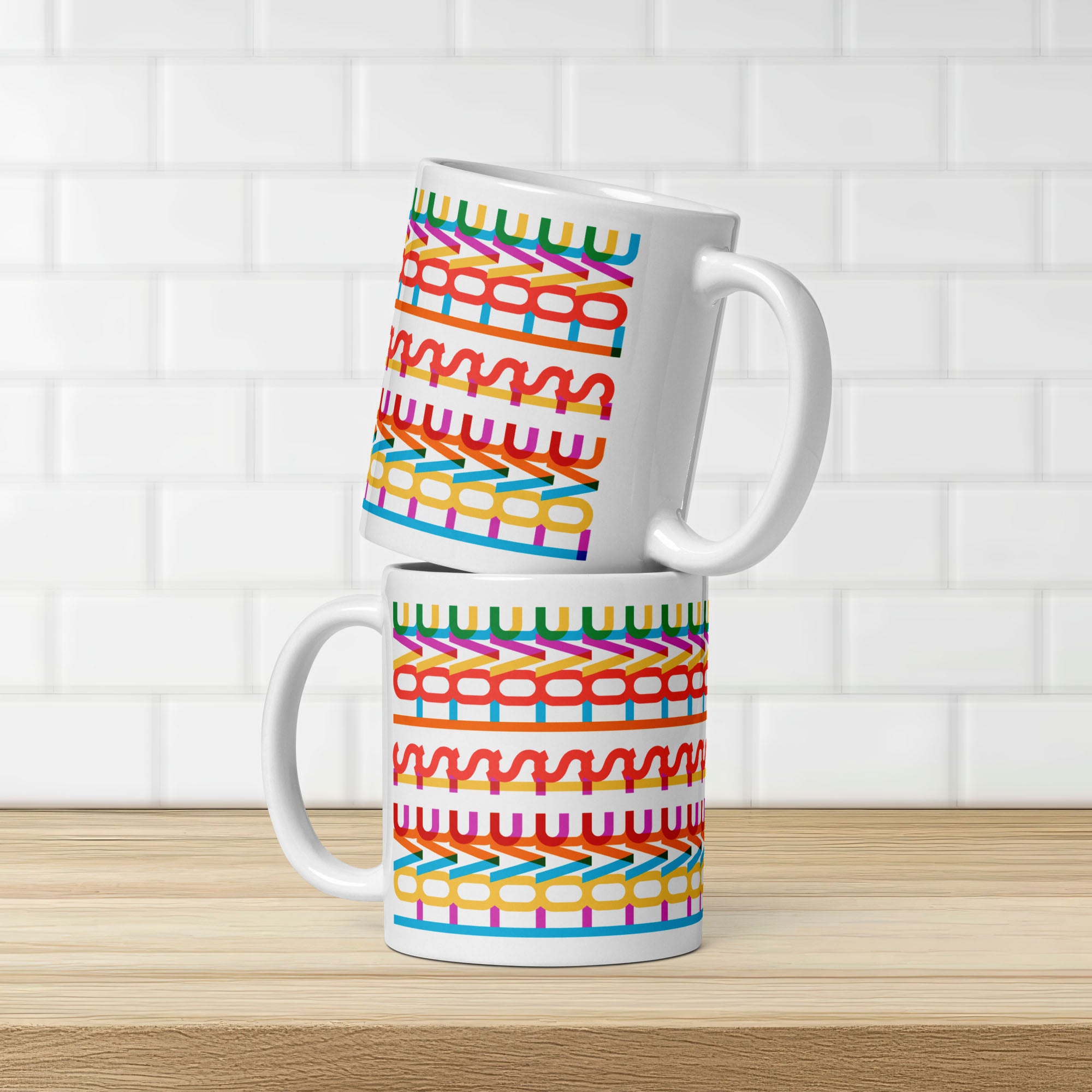 Two stacked colorful coffee mug with a repeating hidden “love is love” message in the Gilbert font, featuring bright rainbow-inspired patterns wrapped around the mug, on a kitchen counter showing both sides of mug.