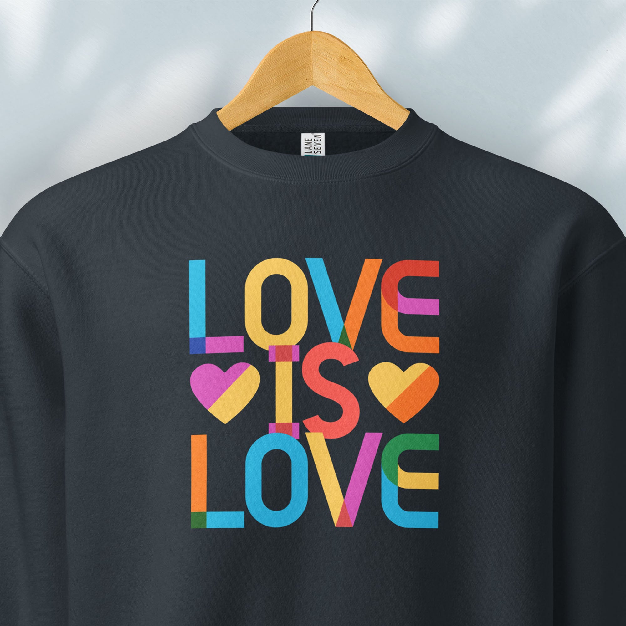 Hanging navy sweatshirt with rainbow “love is love” text designed in the Gilbert font.