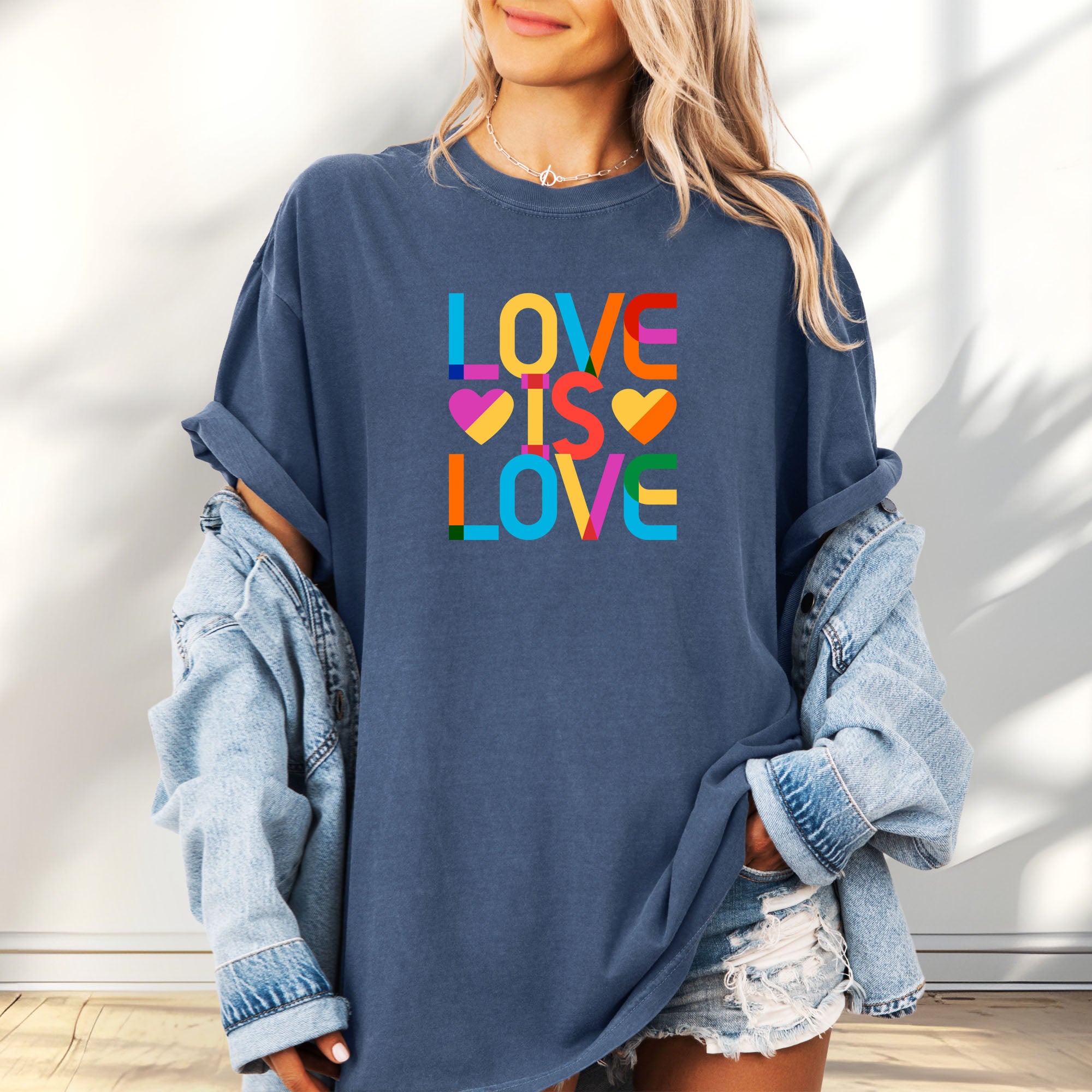 Female model wearing oversized denim t-shirt with rainbow “love is love” text block.