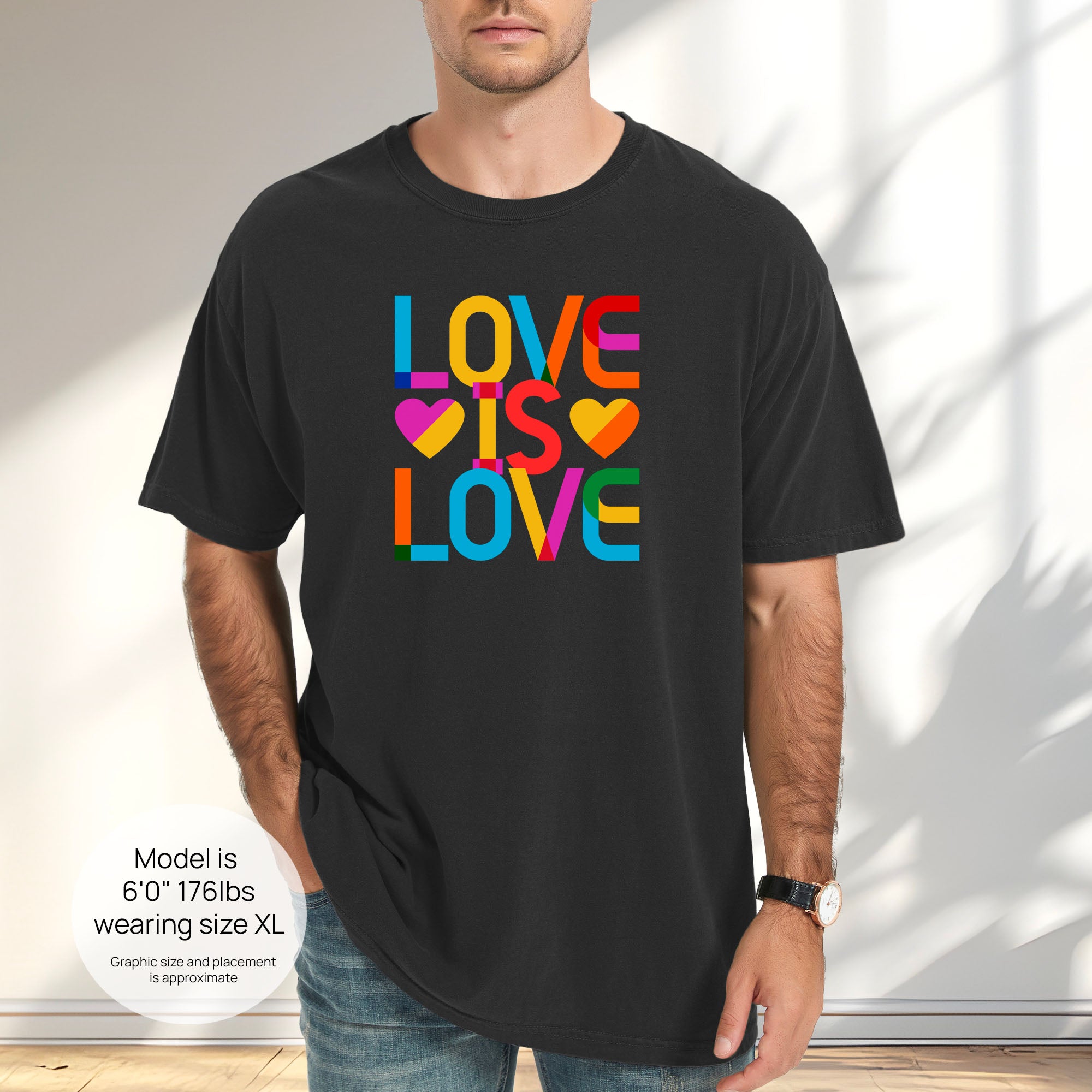 Male model wearing black t-shirt with rainbow “love is love” text block. Includes size and fit information for the model who is 6 feet 0 inches, 176 pounds, and wearing a size XL shirt.
