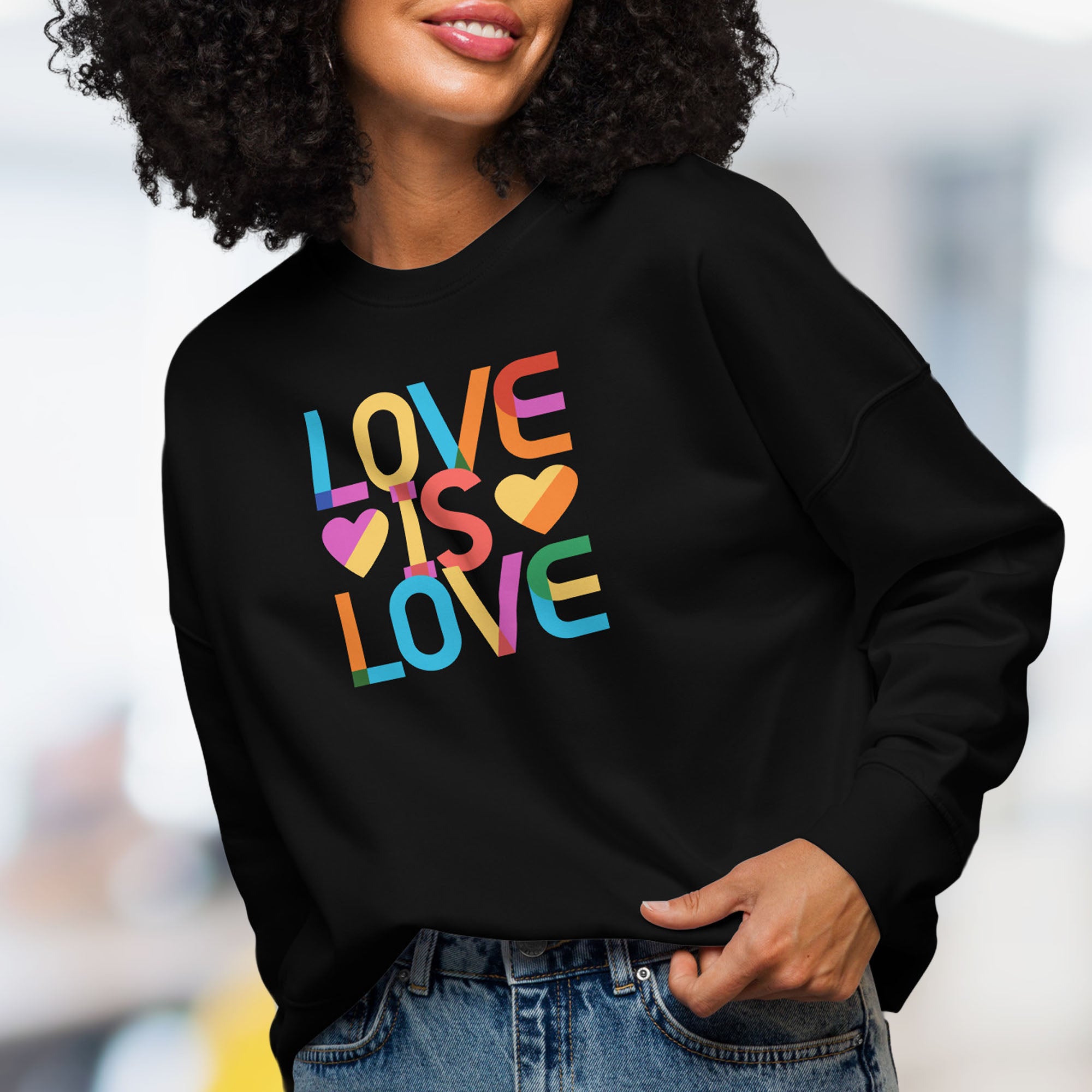 Front view of female model wearing black women's sweatshirt with rainbow “love is love” text designed in the Gilbert font.