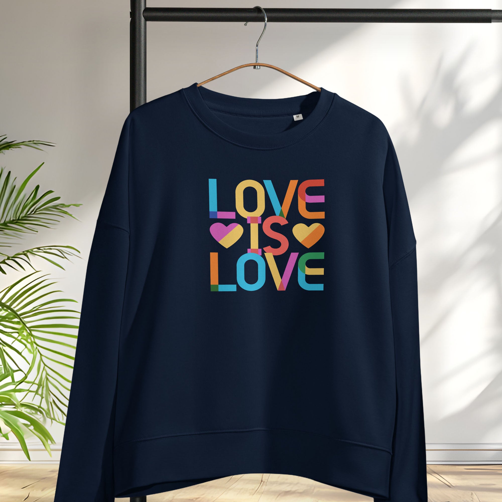 Hanging navy women's sweatshirt with rainbow “love is love” text designed in the Gilbert font.
