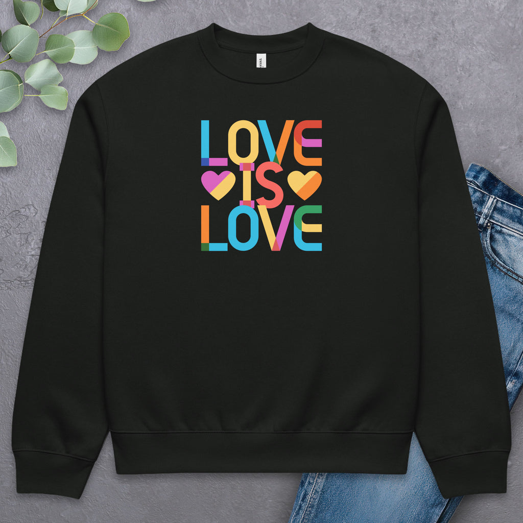 Black t-shirt with rainbow “love is love” text designed in the Gilbert font, laying flat with a pair of jeans and greenery.