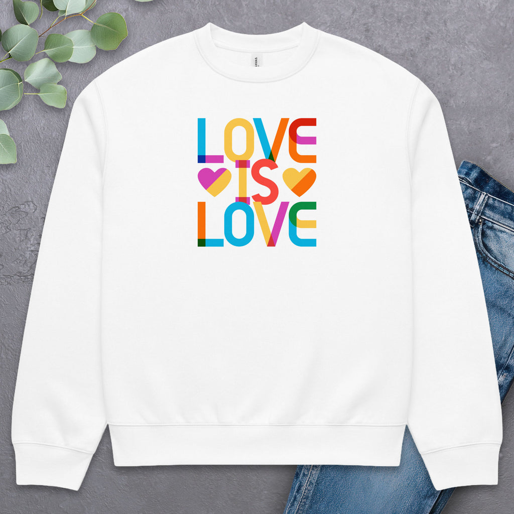 White t-shirt with rainbow “love is love” text designed in the Gilbert font, laying flat with a pair of jeans and greenery.