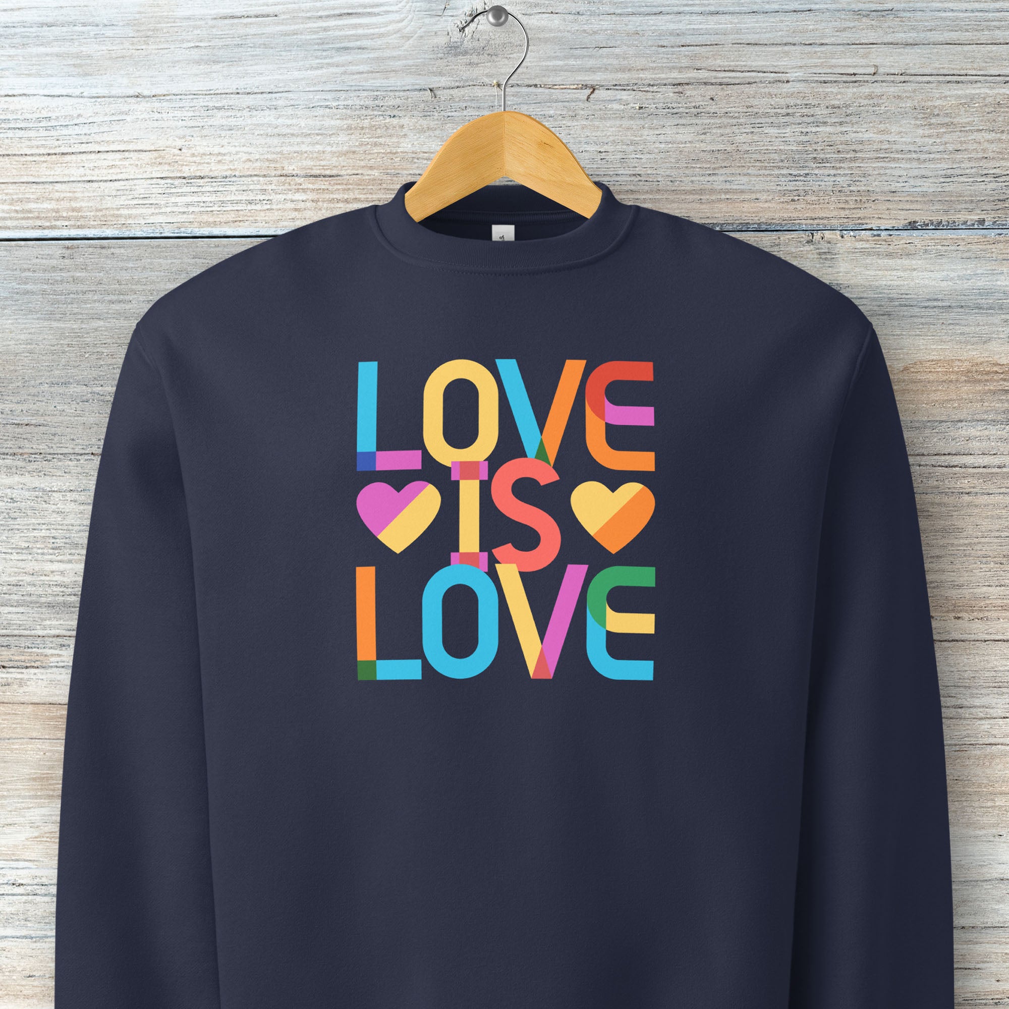 Hanging navy t-shirt with rainbow “love is love” text designed in the Gilbert font.