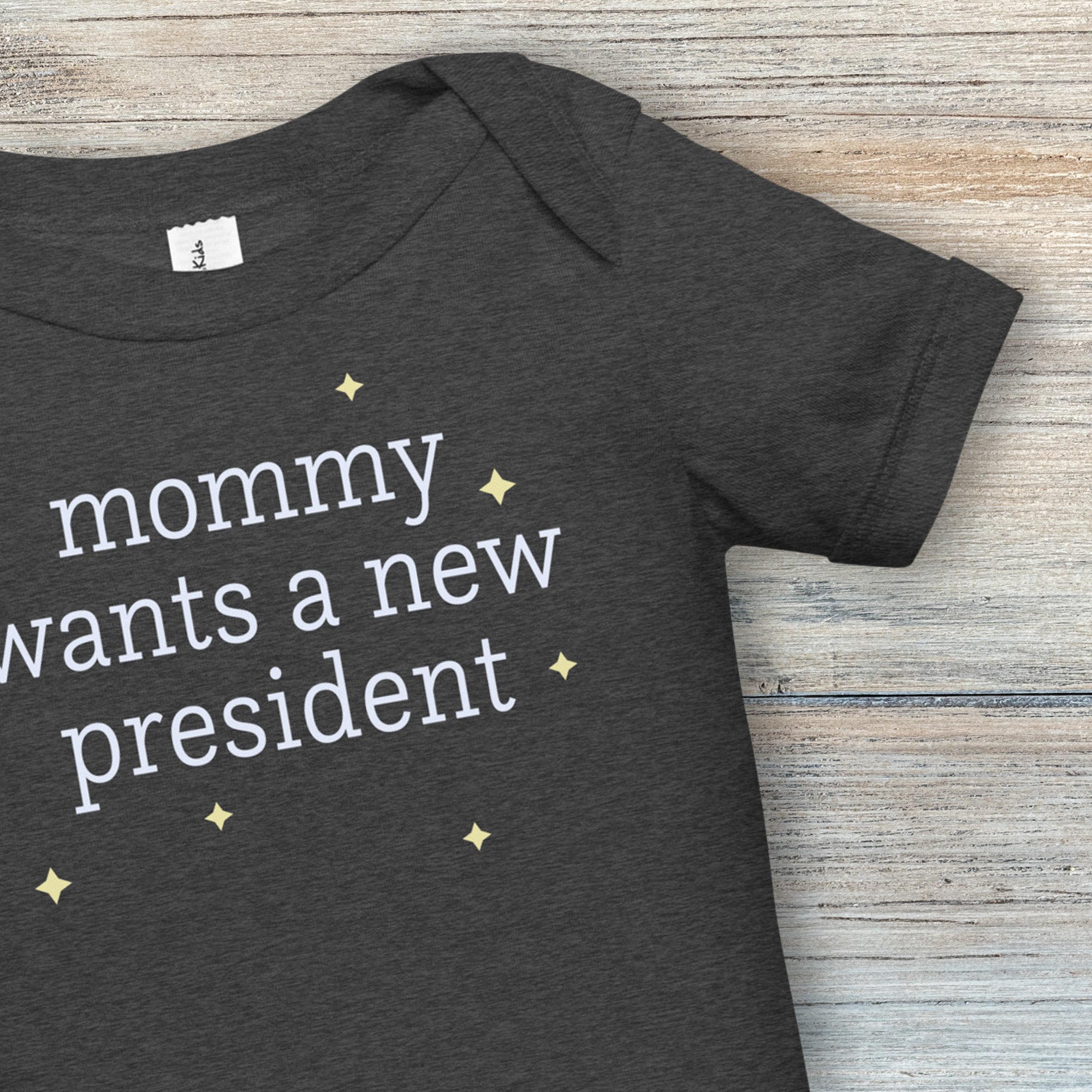 Closeup of neckline and sleeve on dark heather grey baby short sleeve one piece with light text reading “mommy wants a new president."