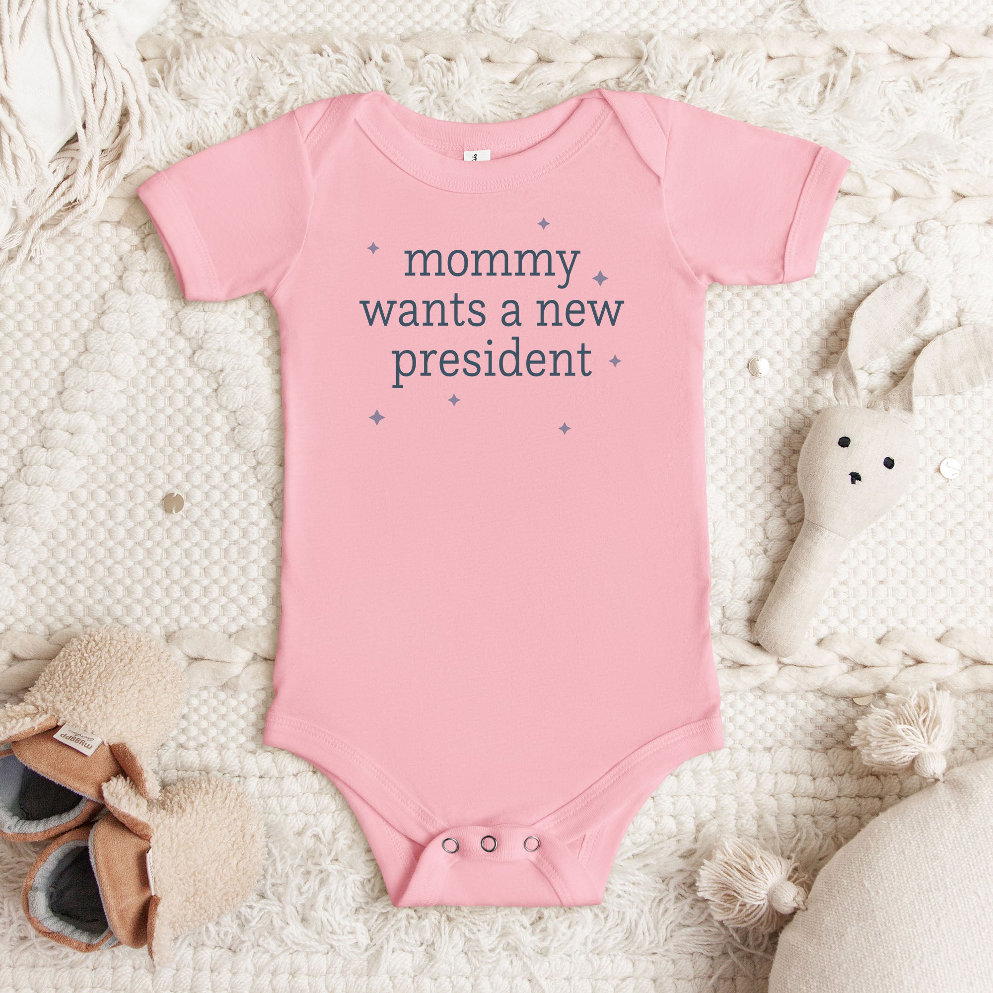 Pink baby short sleeve one piece with dark text reading “mommy wants a new president."
