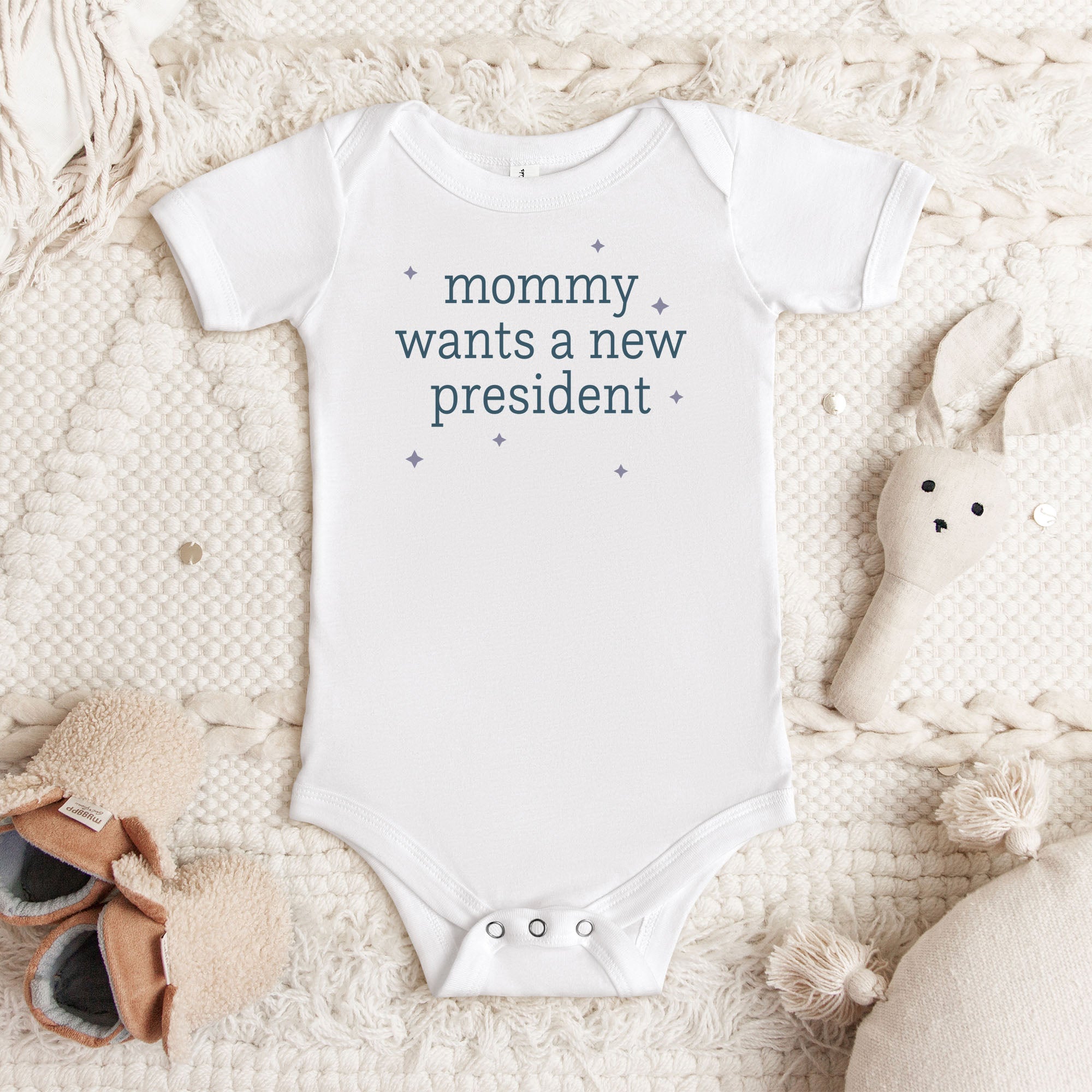 White baby short sleeve one piece with dark text reading “mommy wants a new president."