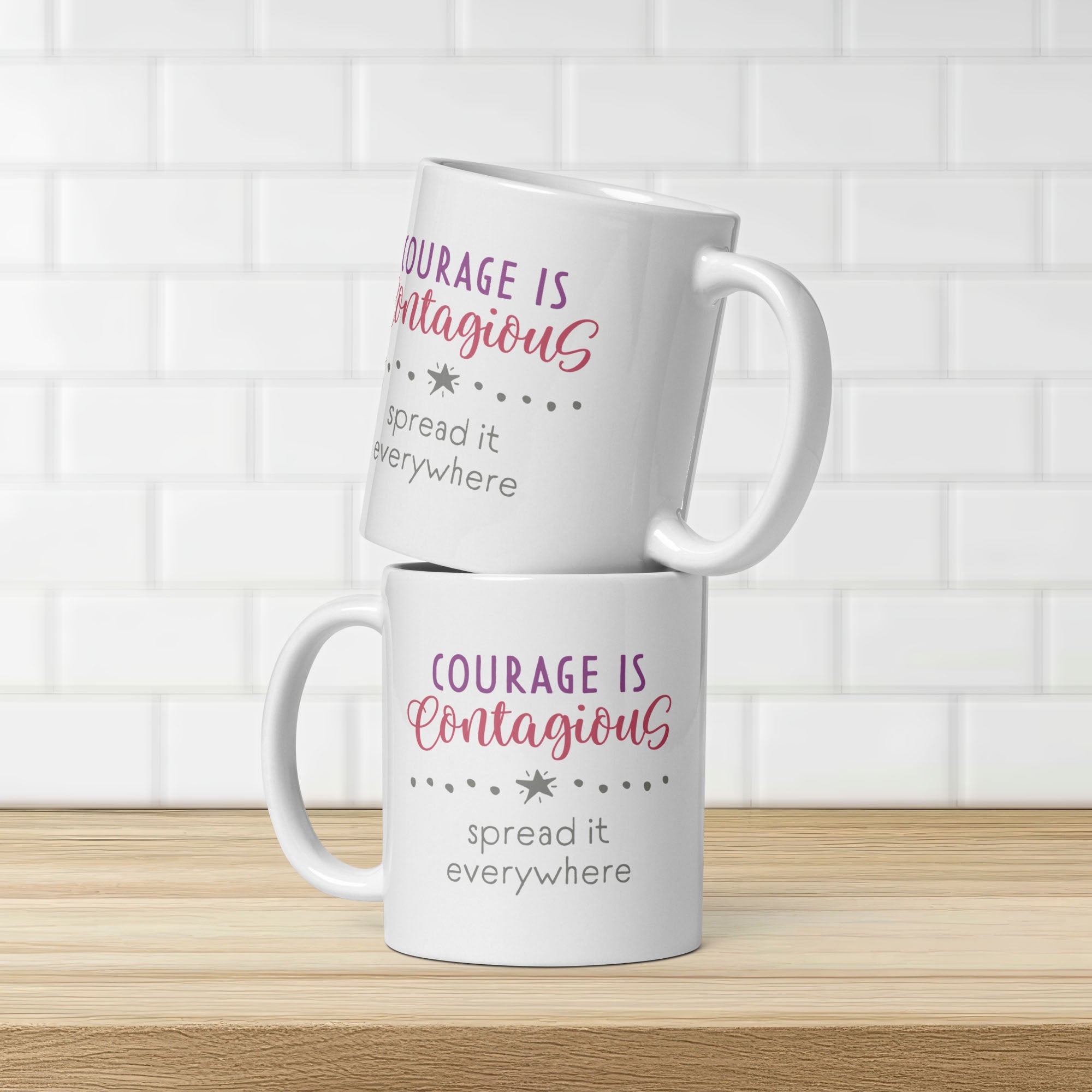 Two stacked mugs on counter with styled text graphic that reads "courage is contagious – spread it everywhere". Graphic is same on both sides of mug.