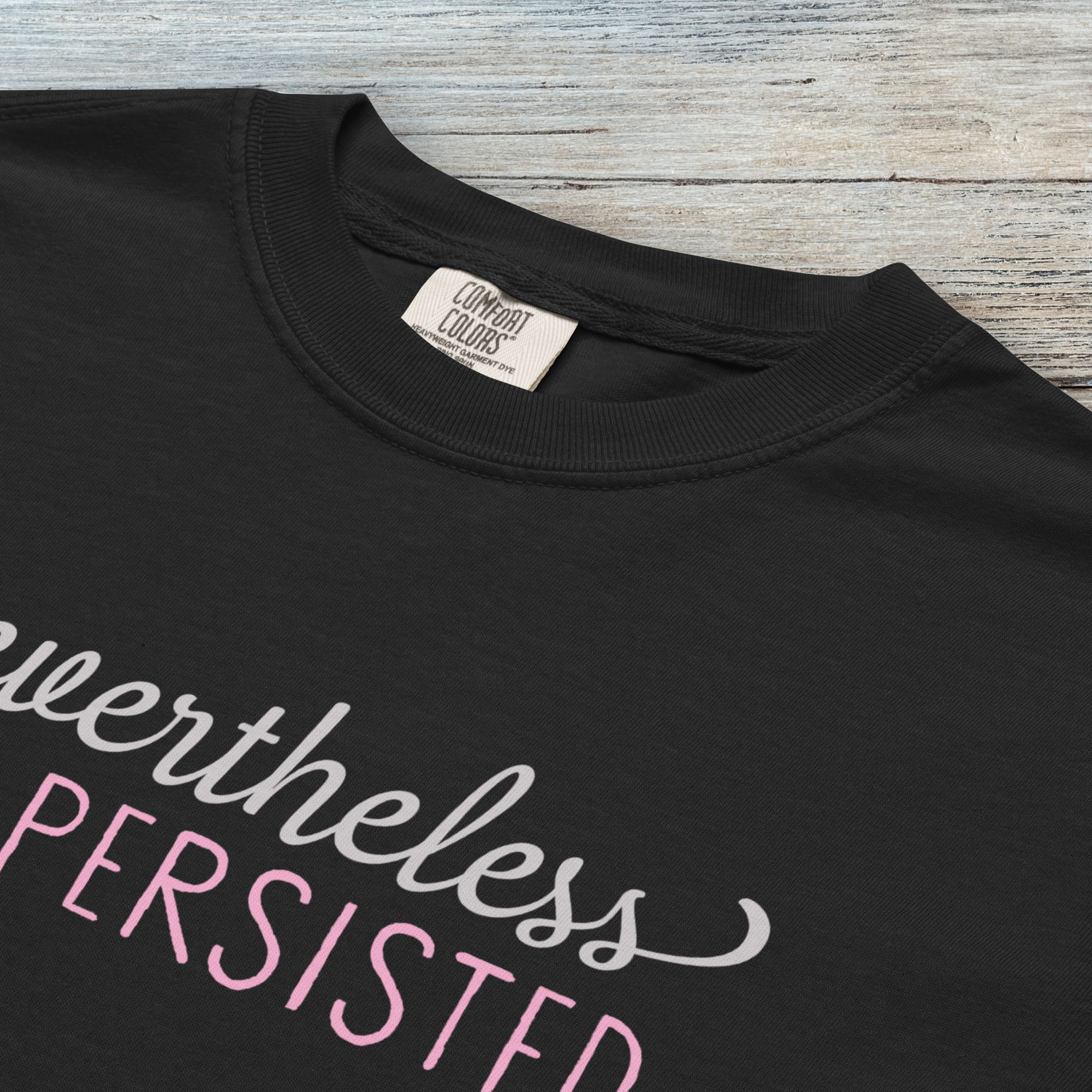 Closeup detail of black Comfort Colors garment-dyed tee with stylized text graphic that reads "nevertheless she persisted."