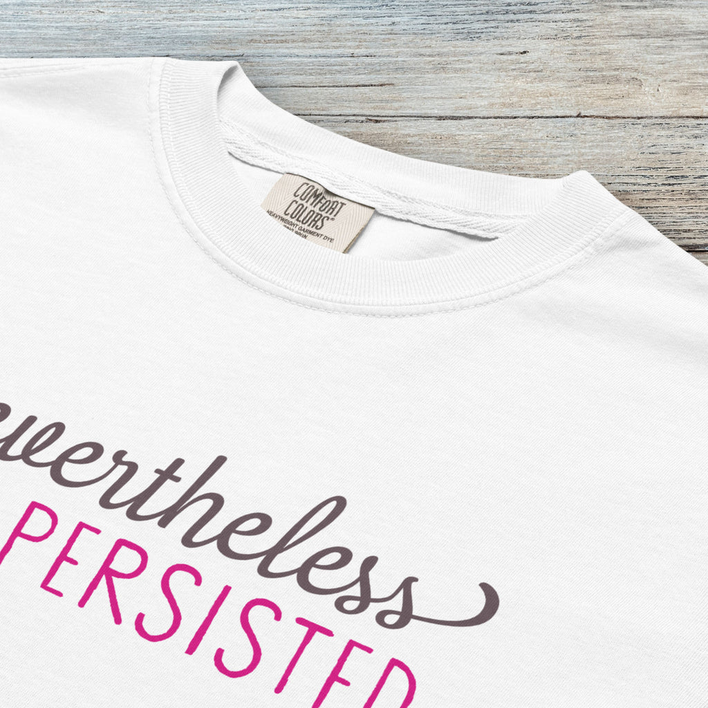 Closeup detail of white Comfort Colors garment-dyed tee with stylized text graphic that reads "nevertheless she persisted."