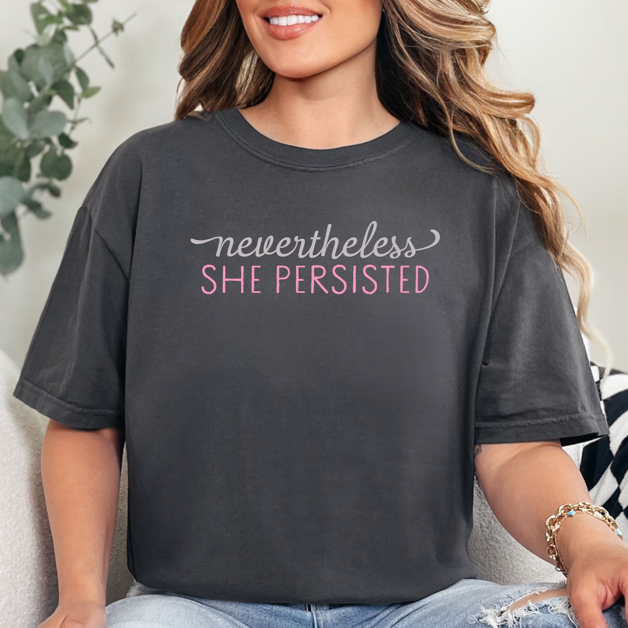Female model wearing graphite Comfort Colors garment-dyed tee with stylized text graphic that reads "nevertheless she persisted."