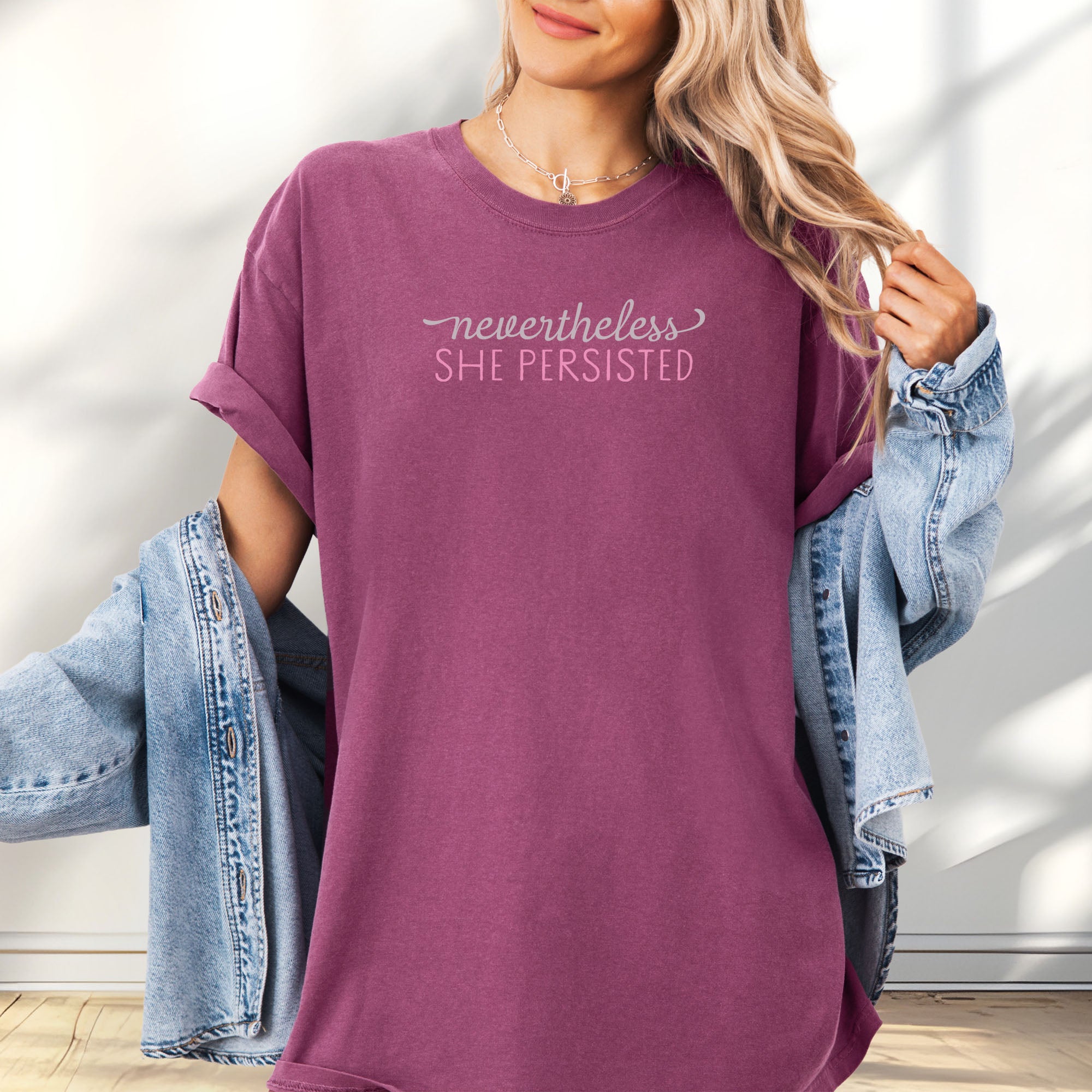 Female model wearing oversized berry Comfort Colors garment-dyed tee with stylized text graphic that reads "nevertheless she persisted."