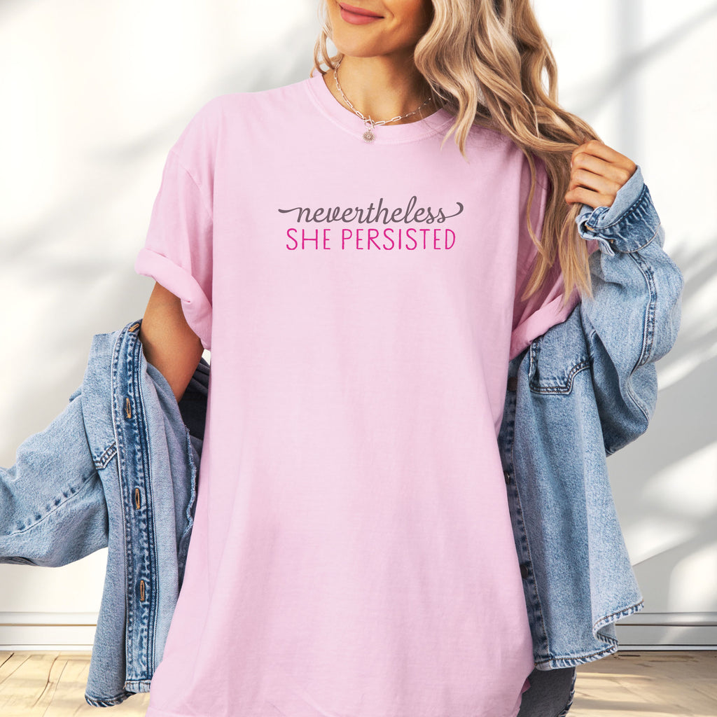 Female model wearing blossom Comfort Colors garment-dyed tee with stylized text graphic that reads "nevertheless she persisted."