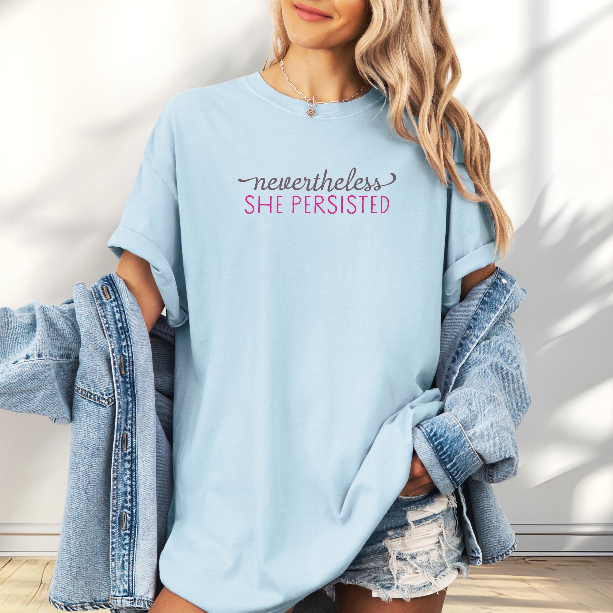 Female model wearing chambray Comfort Colors garment-dyed tee with stylized text graphic that reads "nevertheless she persisted."