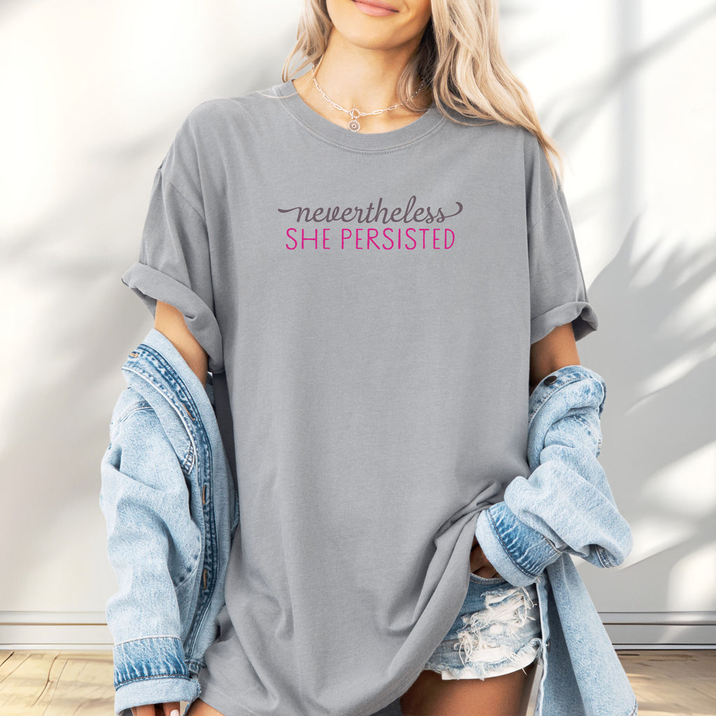 Female model wearing granite Comfort Colors garment-dyed tee with stylized text graphic that reads "nevertheless she persisted."