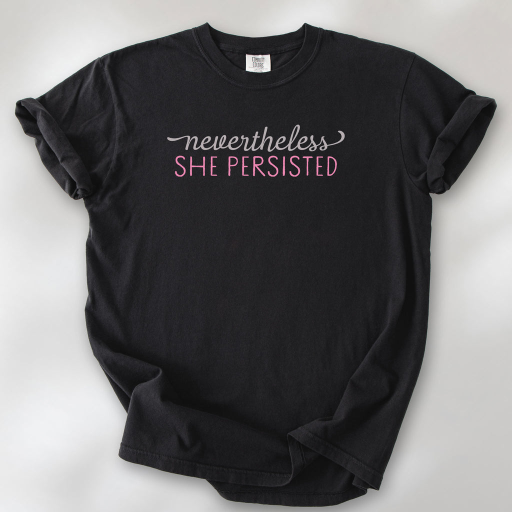 Black Comfort Colors garment-dyed tee with stylized text graphic that reads "nevertheless she persisted."