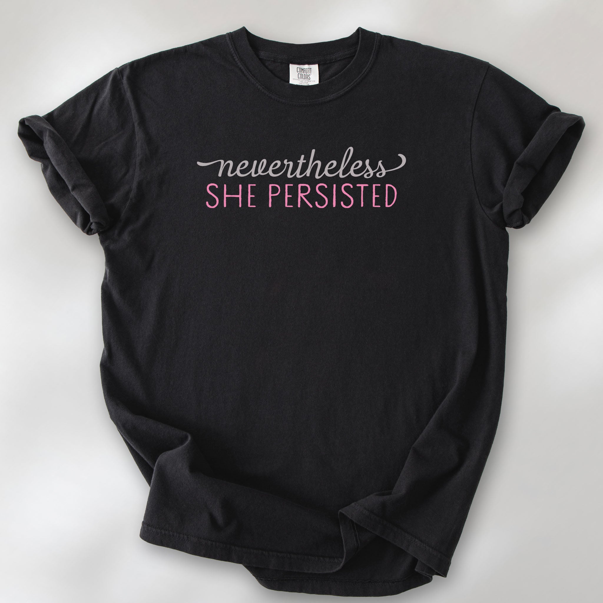 Black Comfort Colors garment-dyed tee with stylized text graphic that reads "nevertheless she persisted."