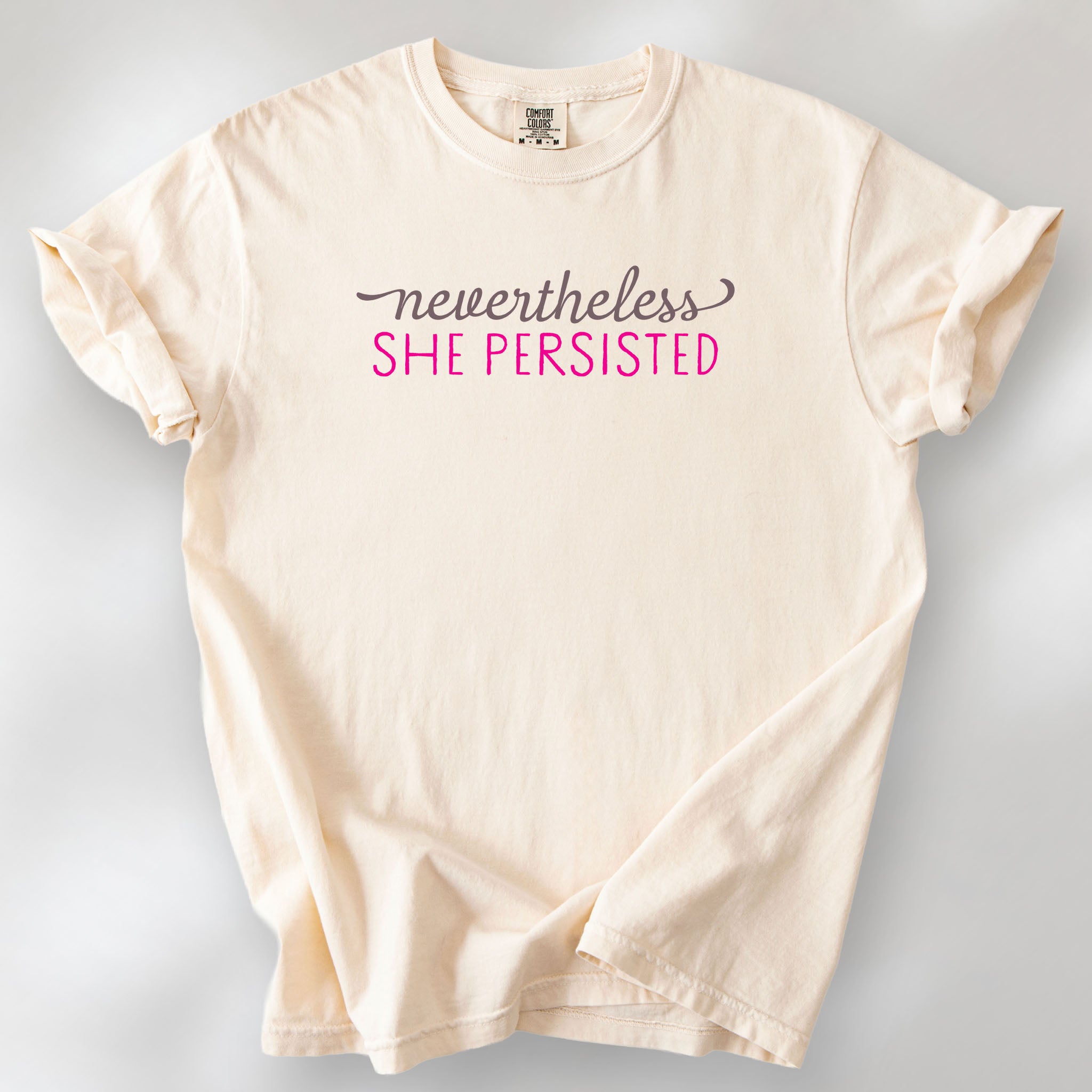 Ivory Comfort Colors garment-dyed tee with stylized text graphic that reads "nevertheless she persisted."
