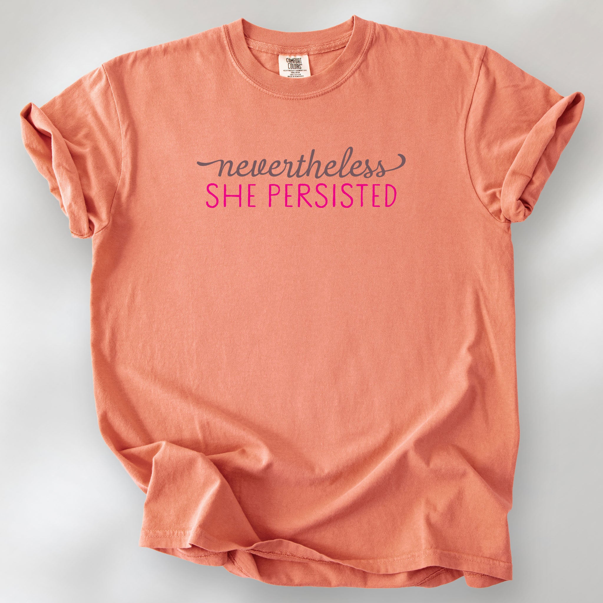Terracotta Comfort Colors garment-dyed tee with stylized text graphic that reads "nevertheless she persisted."