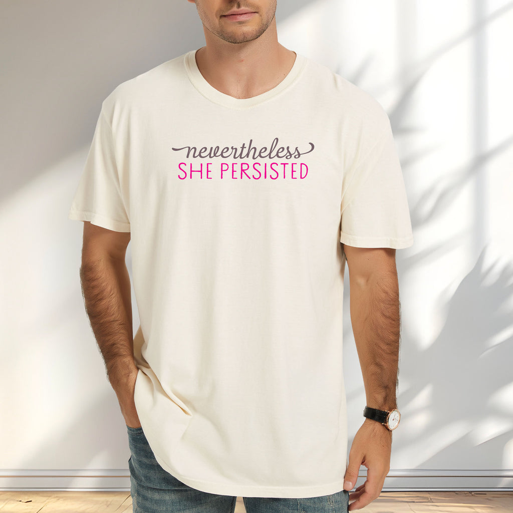 Male model wearing ivory Comfort Colors garment-dyed tee with stylized text graphic that reads "nevertheless she persisted."