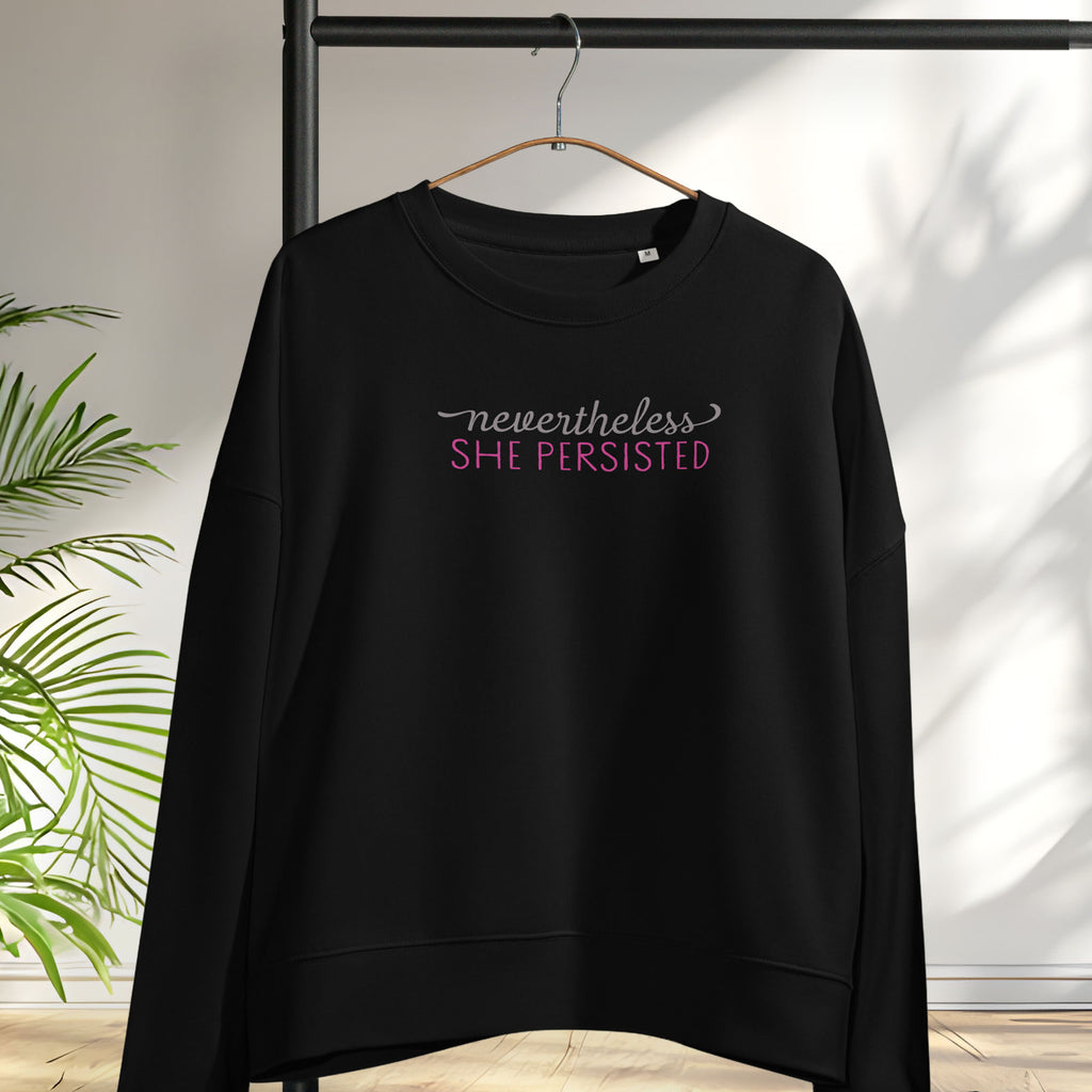 Women's black sweatshirt with styled text that reads "nevertheless, she persisted", hanging on a hanger.