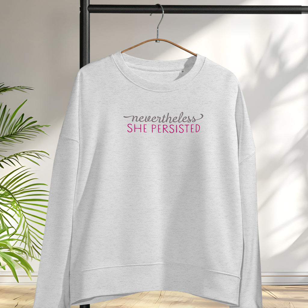 Women's grey sweatshirt with styled text that reads "nevertheless, she persisted", hanging on a hanger.