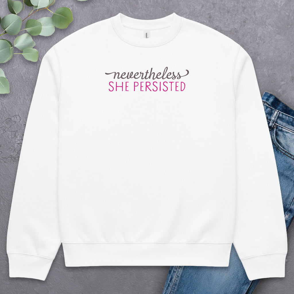 White sweatshirt with styled text that reads "nevertheless, she persisted", laying flat with a pair of jeans.