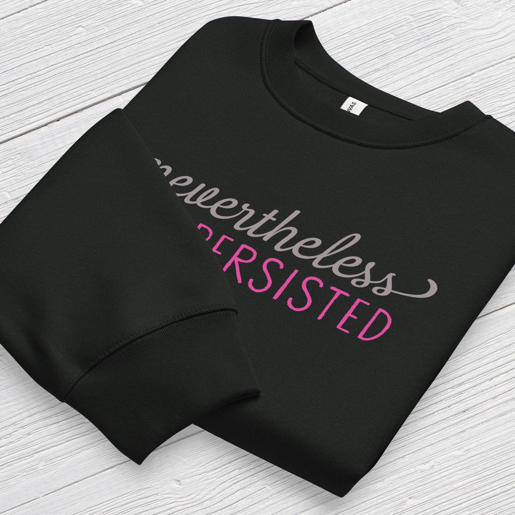 Black sweatshirt with styled text that reads "nevertheless, she persisted", folded flat showing graphic and cuff detail.
